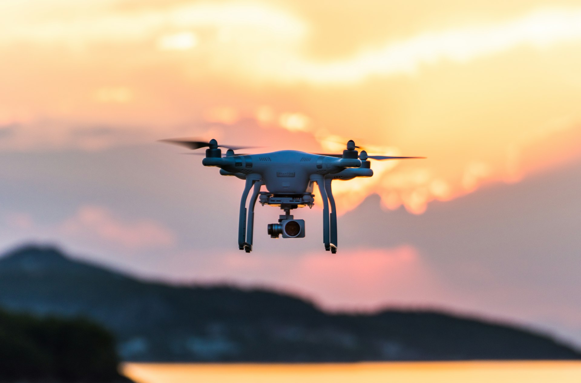 Camera drone hovering at sunset, golden sky over hills